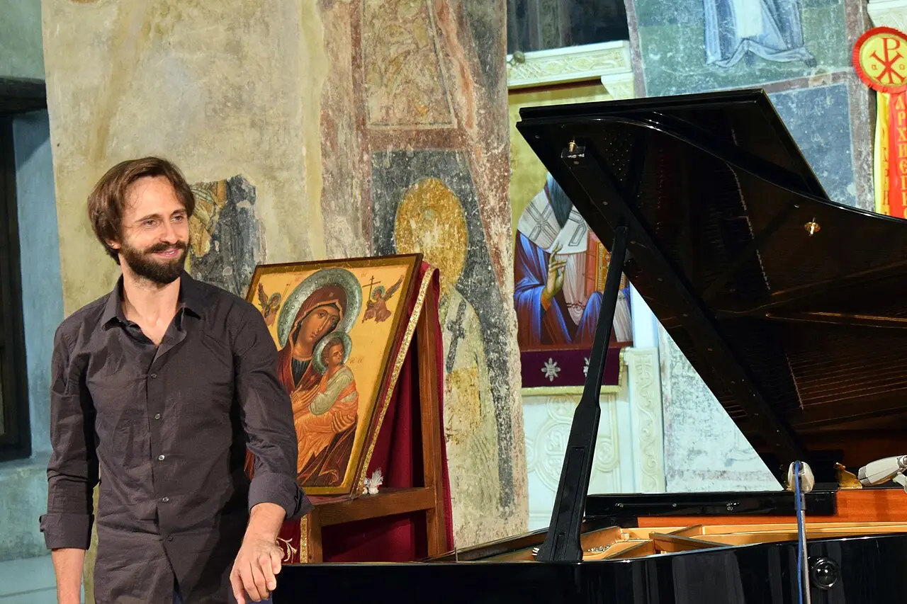 A pianist smiles beside a grand piano inside St Sophia Church, framed by frescoes and an icon