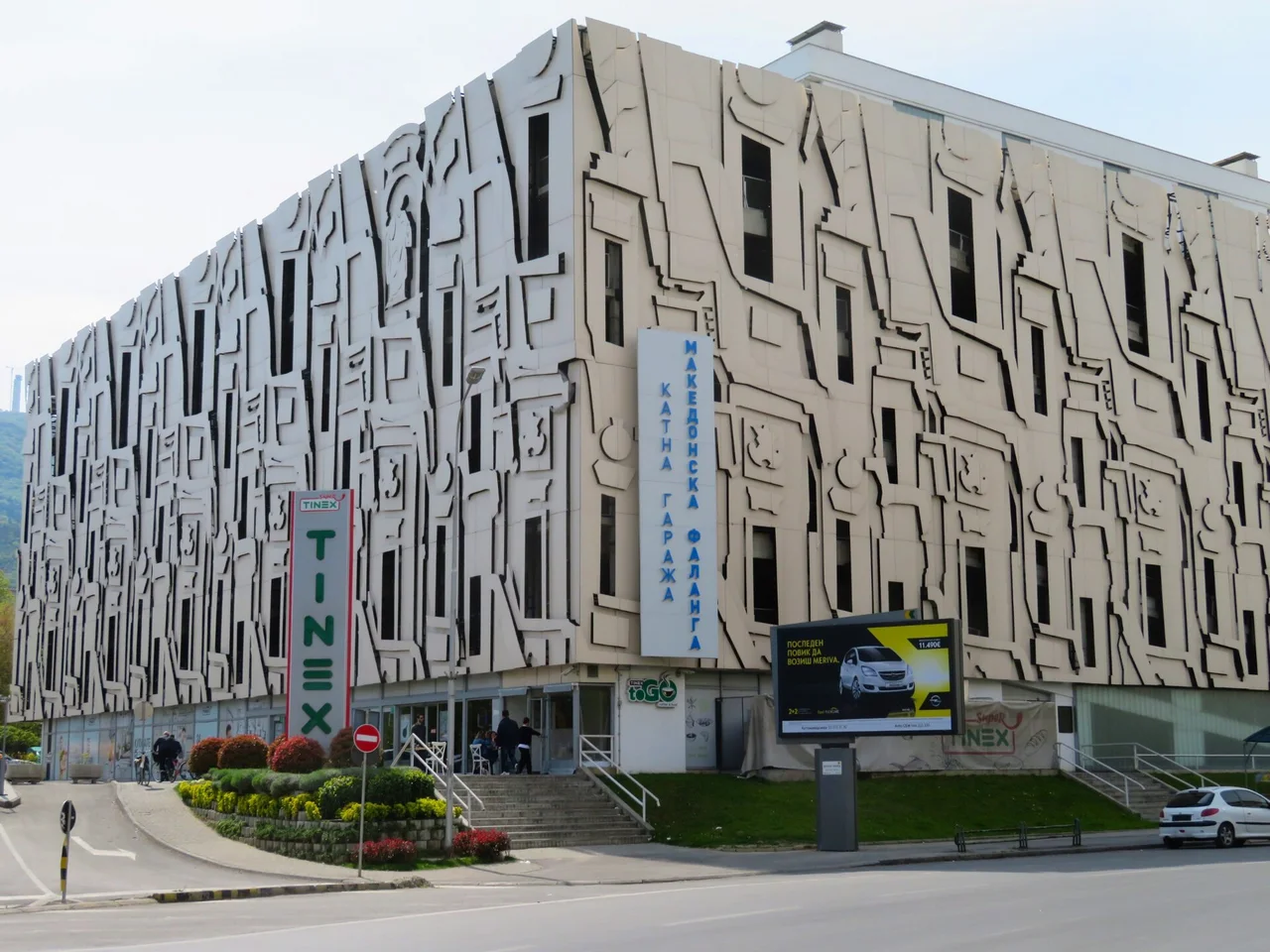 A multi-storey car park in Skopje with a relief facade and a blue sign reading Katna Garaza Makedonska Falanga on its corner