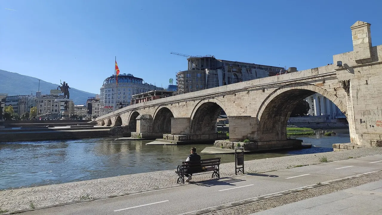 The Stone Bridge over the Vardar in Skopje on a clear day, with Macedonia Square and the Warrior on a Horse statue behind it