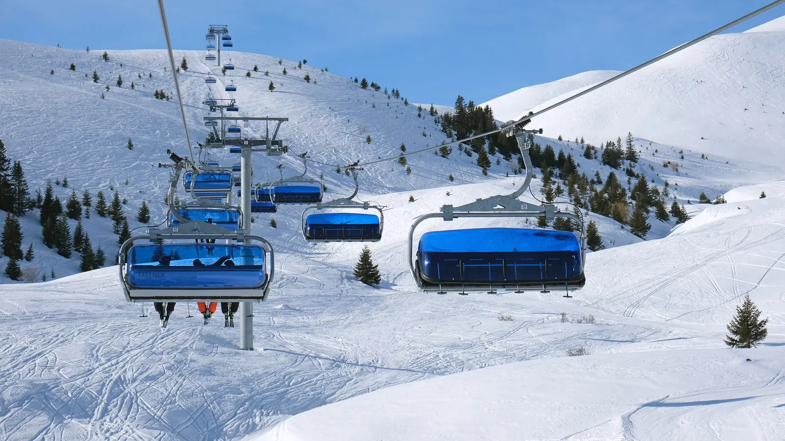 Blue-hooded six-seat chairs of the Popova Šapka express climbing over snowy slopes dotted with pine trees