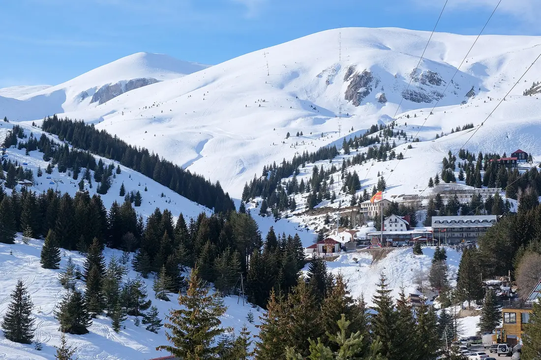 Hotels and chalets at the foot of the snowy slopes of Popova Šapka, with a chairlift line and white peaks above