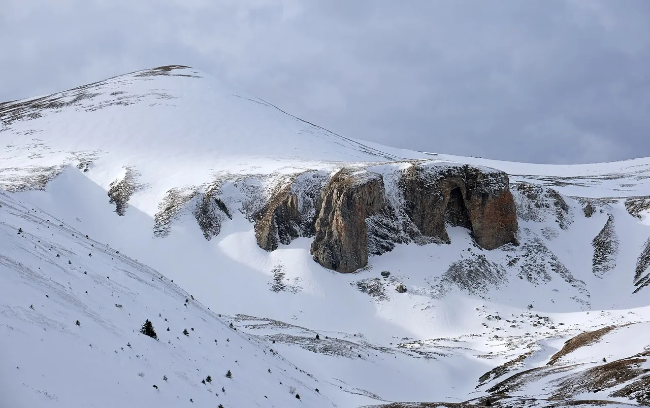 A snow-filled bowl below a wall of brown rock outcrops on the Šar mountains above Popova Šapka