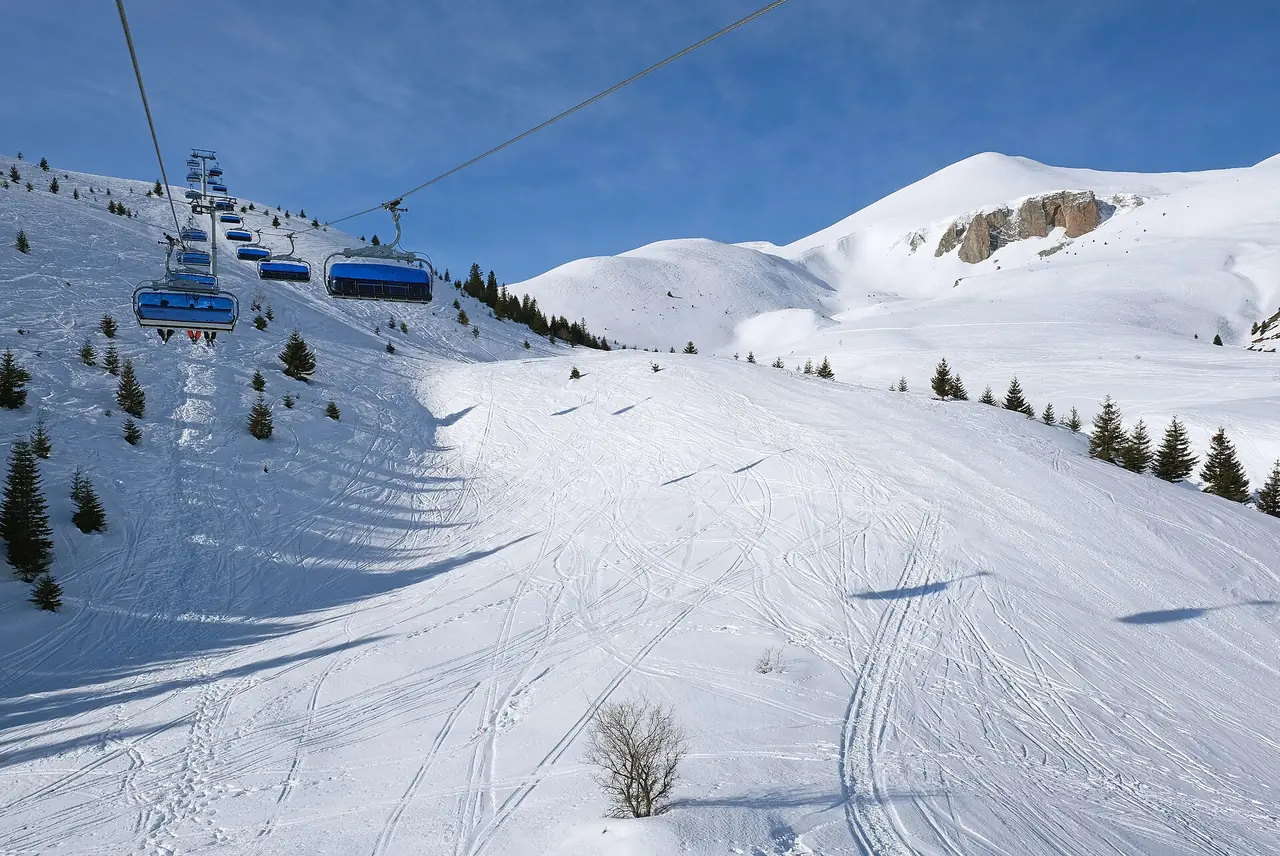 The six-seat chairlift running above a wide groomed piste at Popova Šapka, with a rocky outcrop on the snowy ridge behind