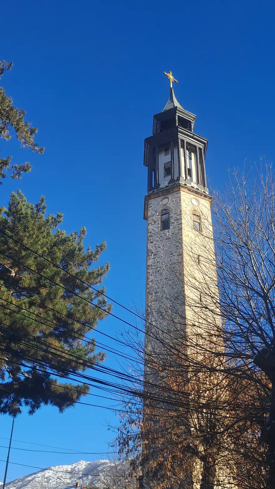 The tall stone 19th-century clock tower of Prilep topped with a cross, a snow-dusted mountain behind