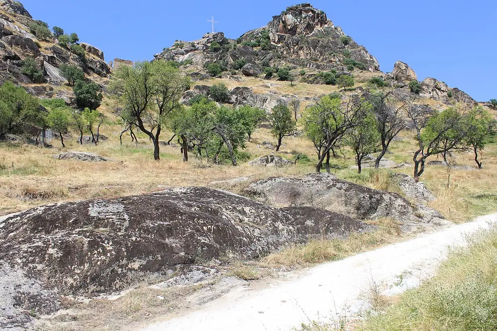 A hillside of huge rounded granite boulders at Markovi Kuli above Prilep, with a summit cross and gnarled trees