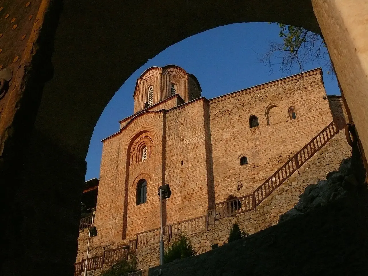 The brick Byzantine church of St Michael the Archangel monastery at Varoš, Prilep, glowing in golden light beneath an arch
