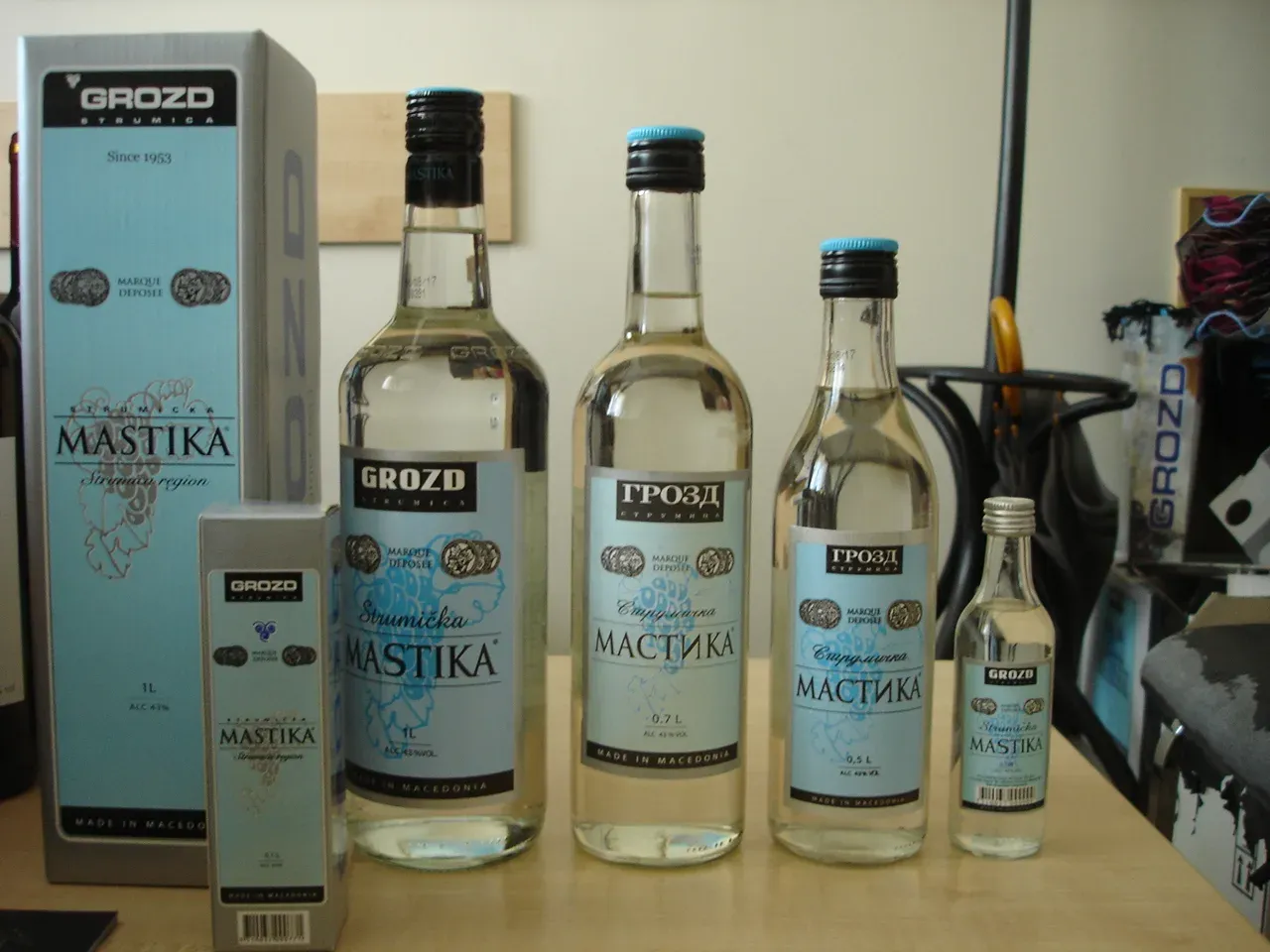Several bottles of Grozd mastika in different sizes with a boxed gift set and a miniature bottle on a wooden shelf