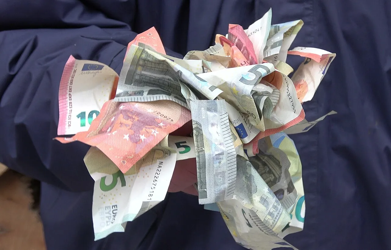 A handful of folded euro banknotes of various denominations held in one hand