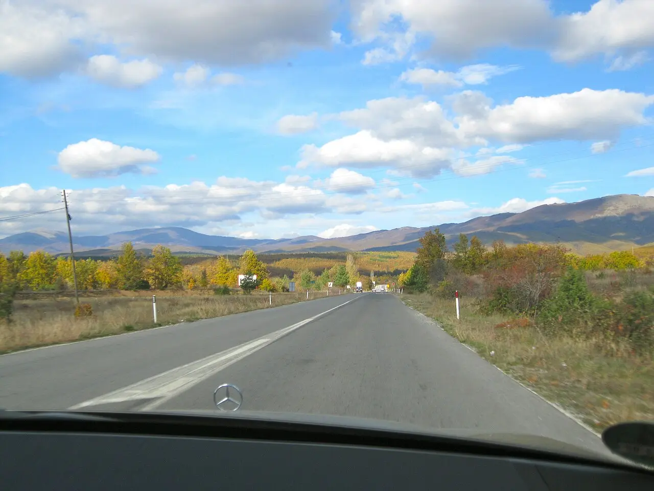 A driver's-eye view through a windscreen of a Macedonian road with autumn mountains ahead