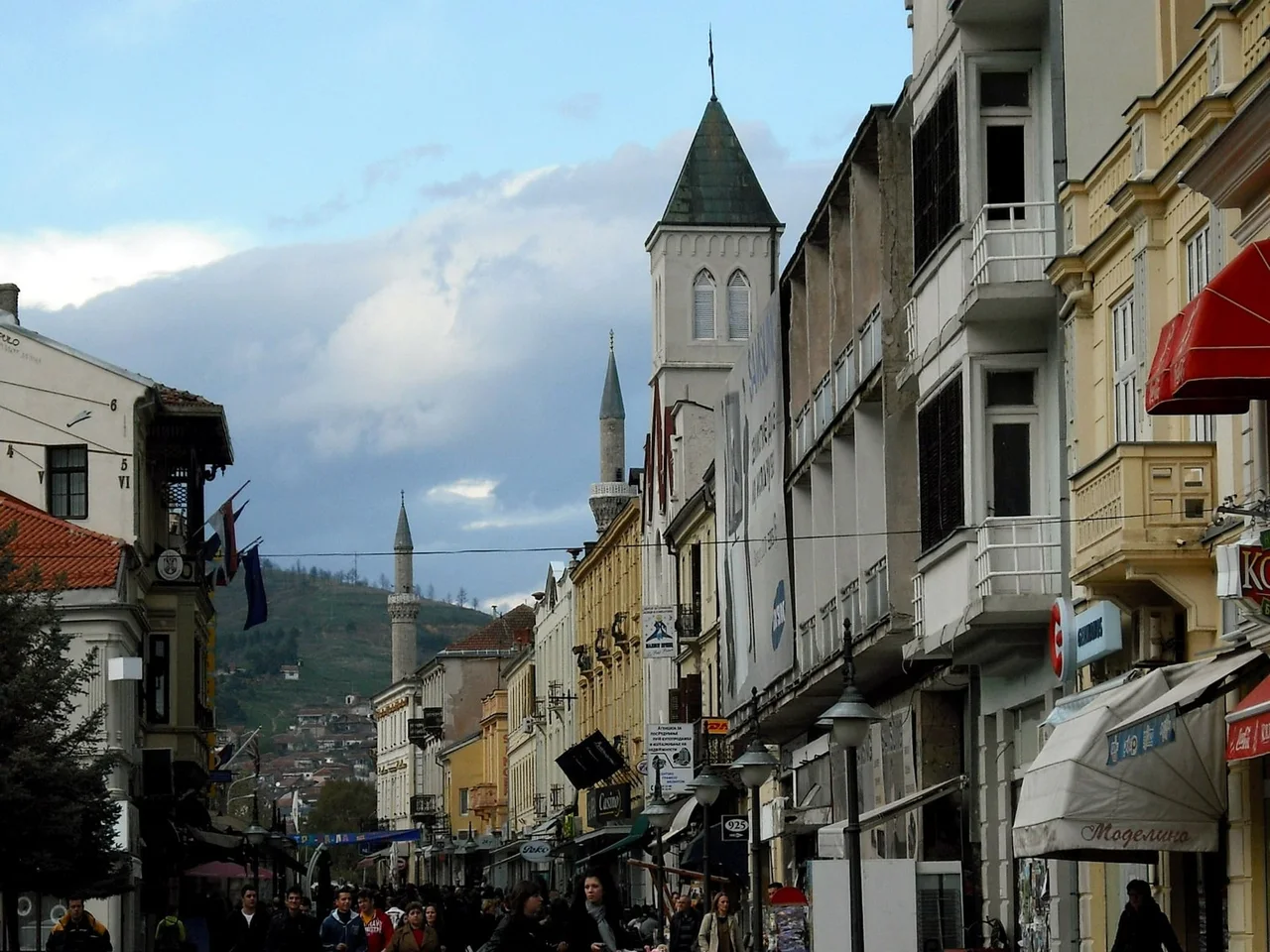 Shirok Sokak, Bitola's pedestrian street, lined with old townhouses and awnings and crowded with walkers, with a church tower and two minarets rising above the rooftops