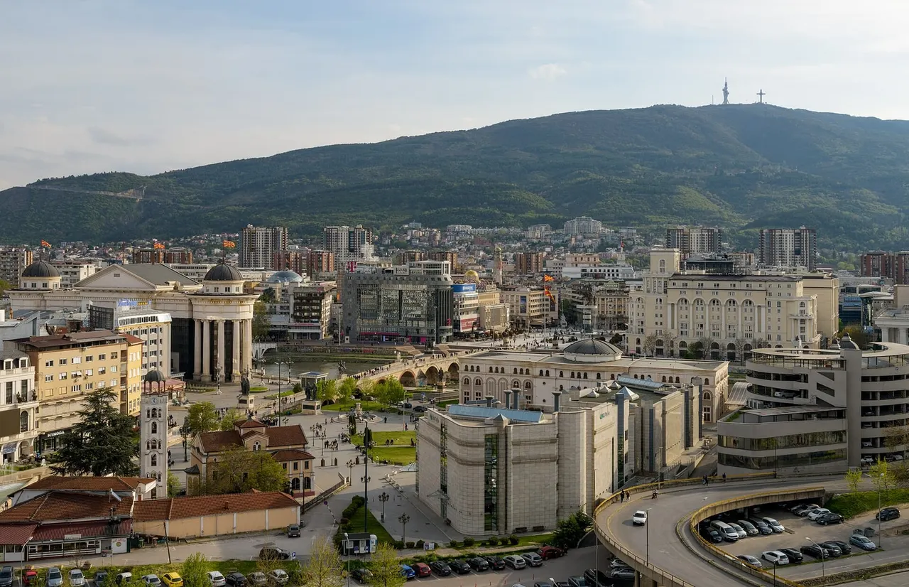 Central Skopje seen from the fortress hill: Macedonia Square and the Stone Bridge over the Vardar in the middle distance, apartment blocks climbing the slope and Mount Vodno with its cross behind
