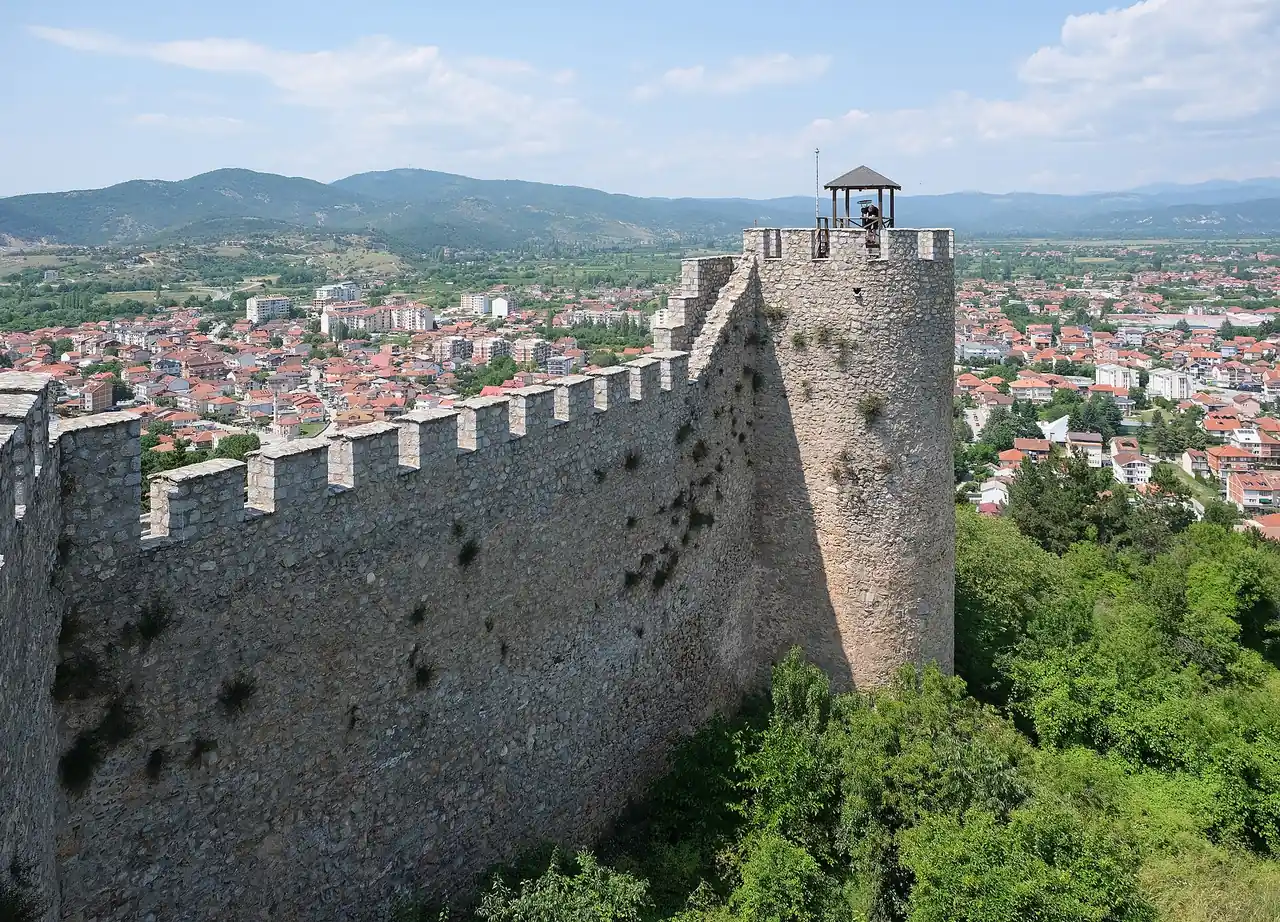 A crenellated stone wall and round tower of Samuel's Fortress above the red roofs of Ohrid