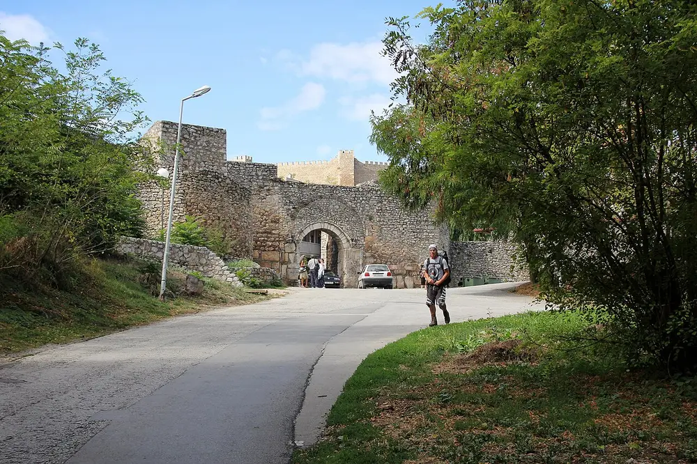 The arched stone Upper Gate of Samuel's Fortress with a lane leading up to it and a walker approaching