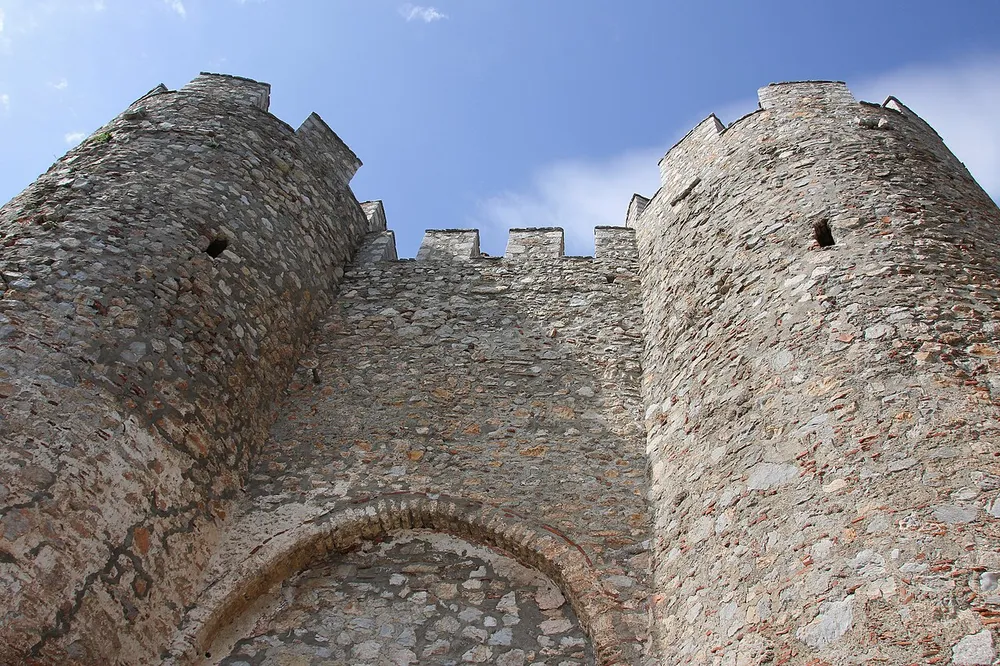 Looking up at two round towers and a battlemented curtain wall of Samuel's Fortress against a blue sky