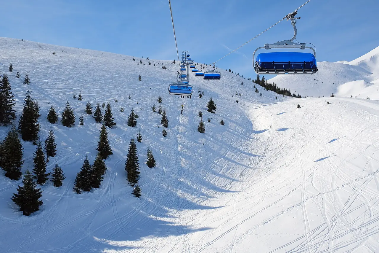 Blue-hooded six-seat chairs climbing over a groomed piste at Popova Šapka with scattered pine trees