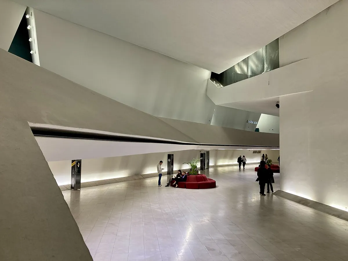 The angular white foyer of the National Opera and Ballet in Skopje, with red seating and people crossing the marble floor