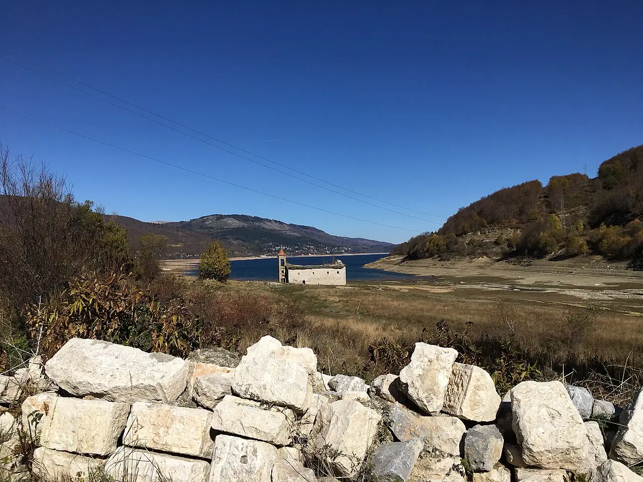 The sunken church of Mavrovo standing on the exposed lakebed when the reservoir is low, with a dry-stone wall in the foreground