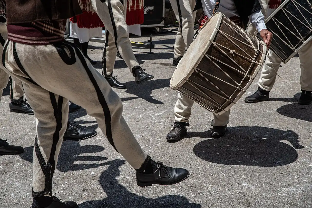 Men in traditional Mijak costume dancing with a large drum at the Galicnik Wedding festival
