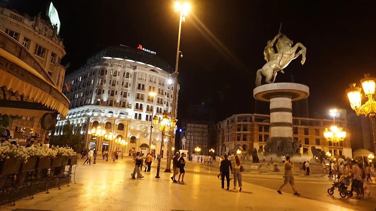 Macedonia Square in Skopje lit up at night with people out by the Warrior on a Horse fountain