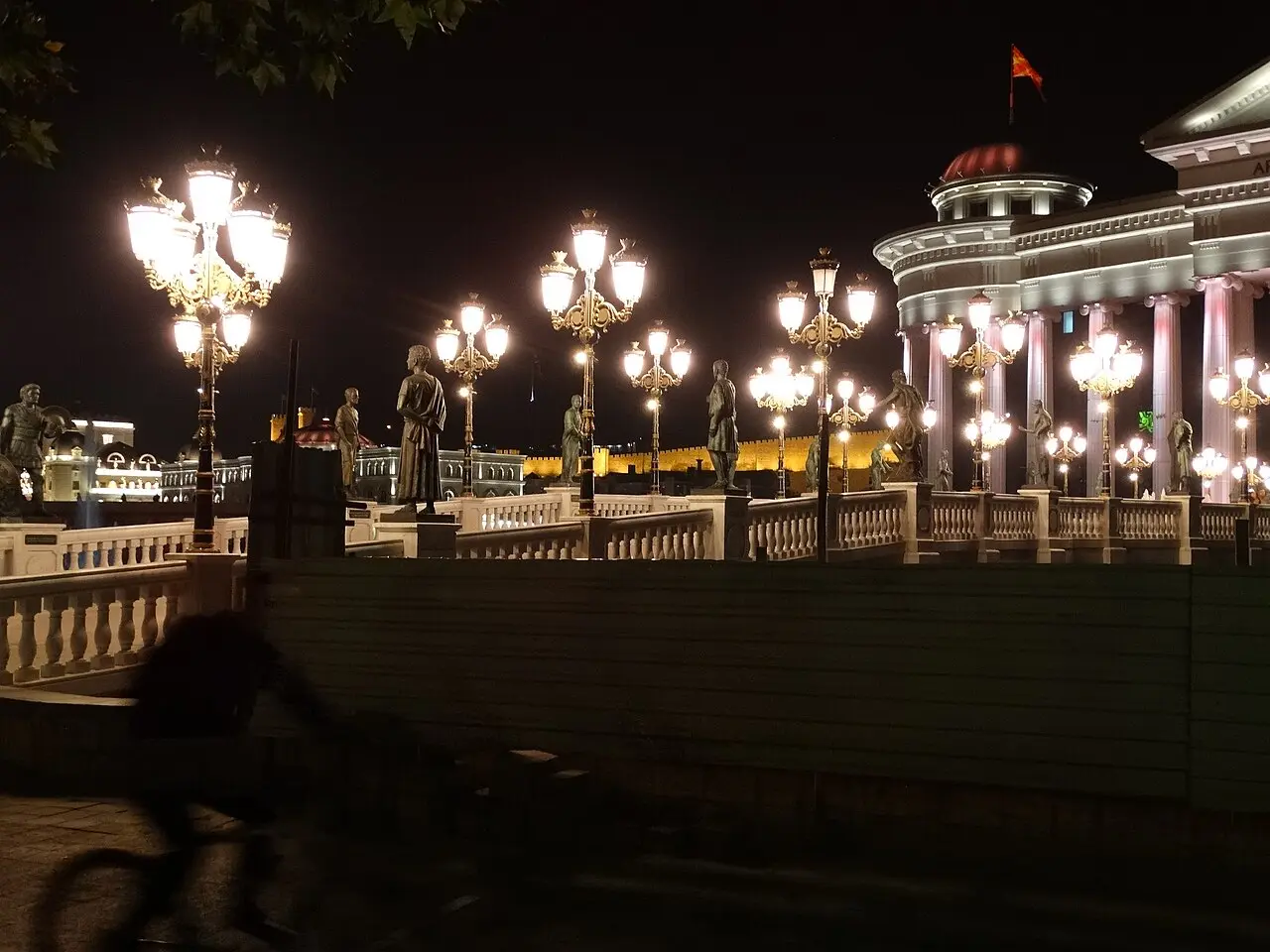 The Vardar riverfront in Skopje at night with ornate street lamps and statues