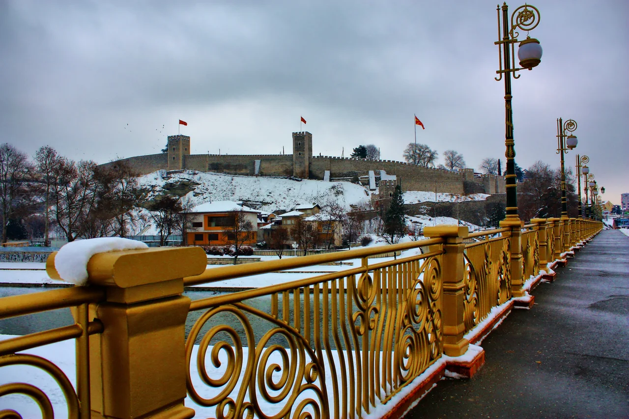 The Kale fortress on its hill above the Vardar, seen from the snow-dusted golden railing of the Goce Delchev Bridge