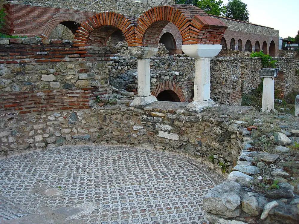 A circular geometric mosaic floor beside brick arches and columns at Heraclea Lyncestis near Bitola