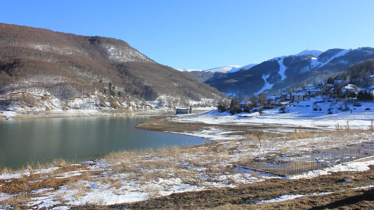 Lake Mavrovo in winter at low water, the sunken church of St Nicholas on the exposed bed and the ski runs of Bistra above Mavrovo village