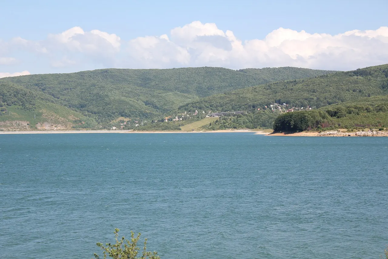 Blue water of Lake Mavrovo in summer with forested hills and the village of Leunovo on the far shore