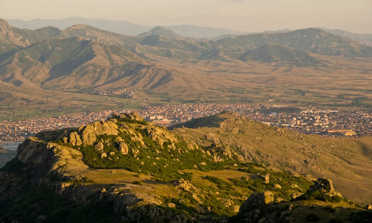 The town of Prilep spread across a plain below boulder-covered hills and mountain ridges, in low golden sunlight