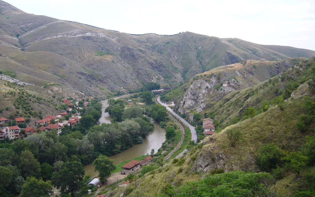 The Vardar river winding through a green gorge near Veles, with a road and a railway line running along the bank