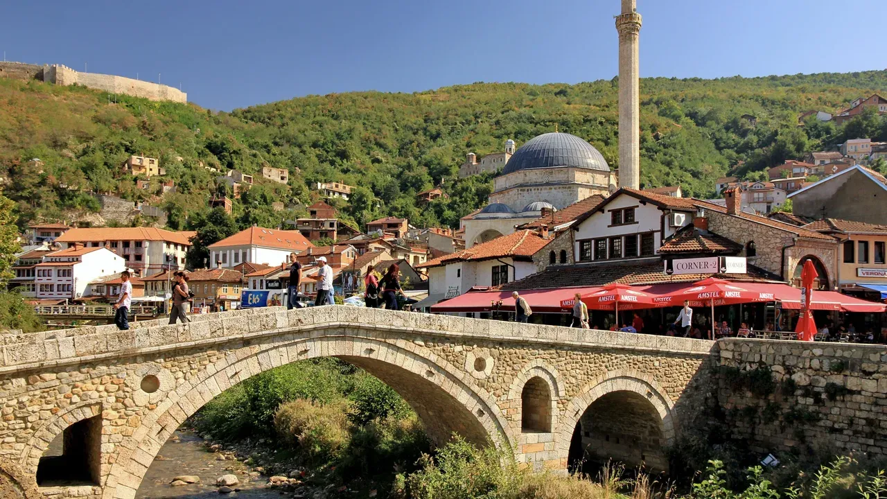 The old stone bridge in Prizren with the Sinan Pasha Mosque, its tall minaret and the hillside town behind it