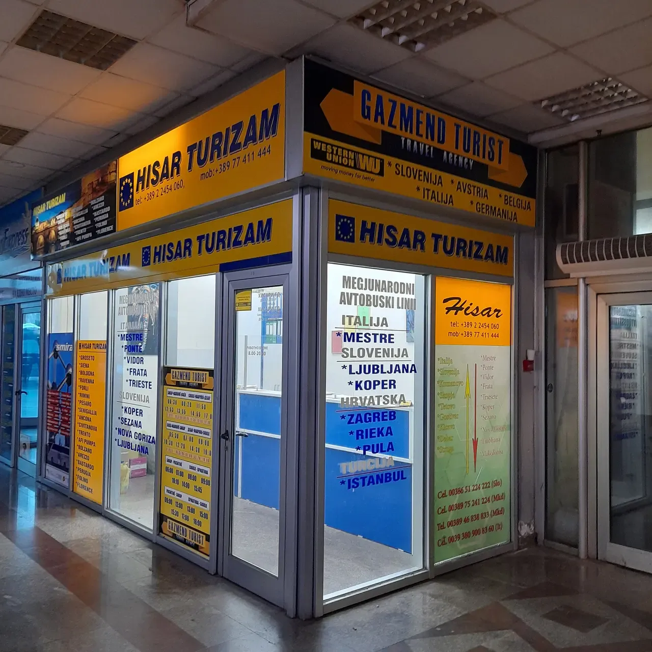 Yellow and blue international bus ticket booths of Hisar Turizam and Gazmend Turist inside a bus station