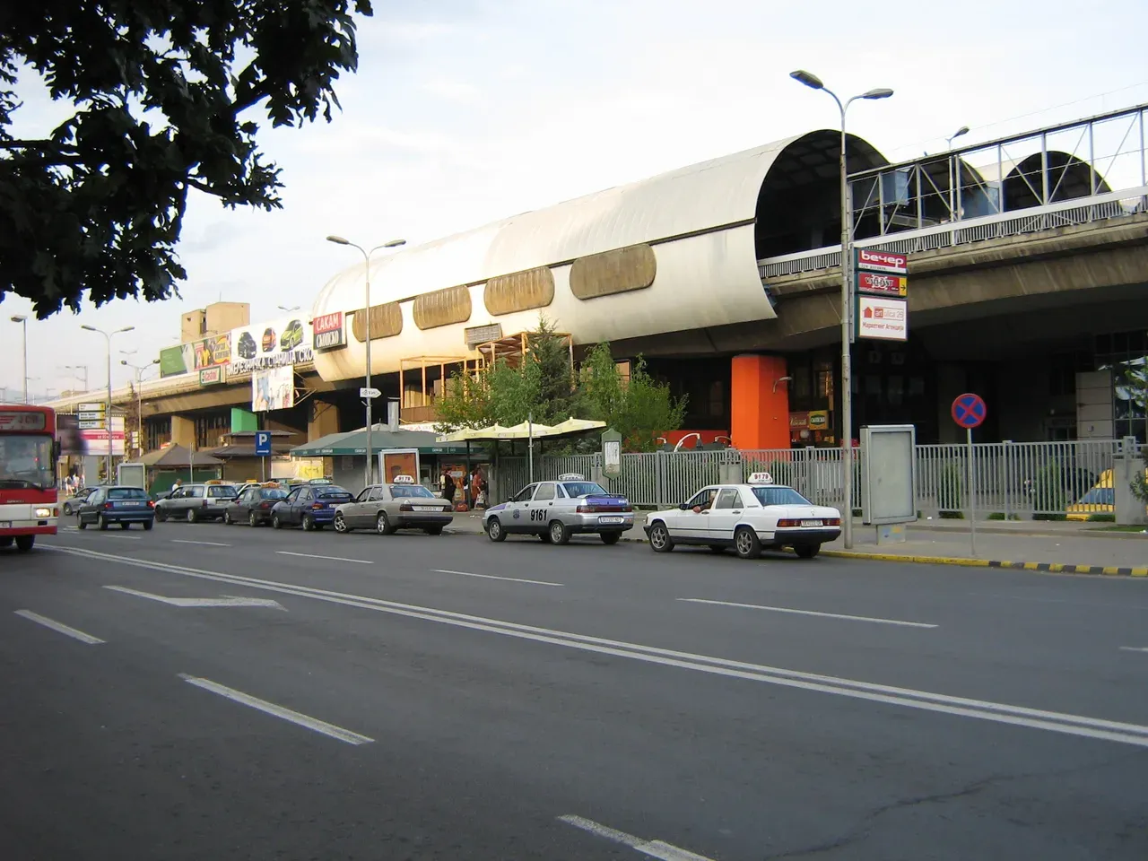 The long low building of the Skopje bus station seen from the road, with cars parked along the kerb