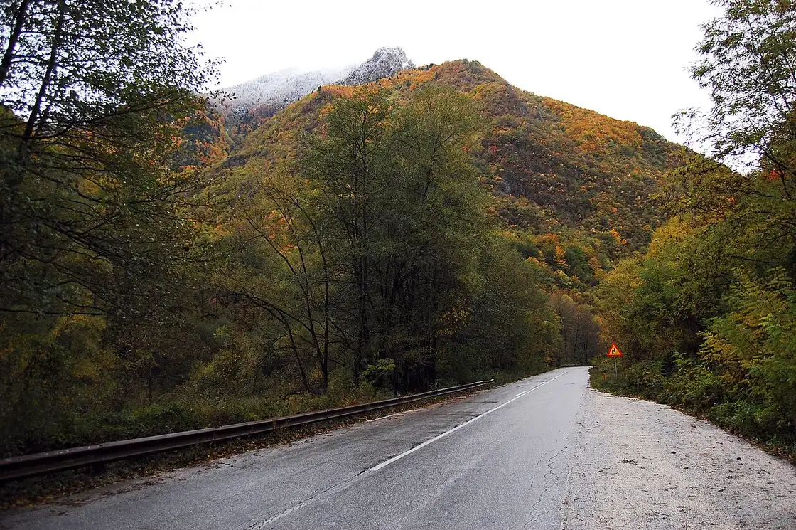 Two-lane mountain road heading toward Debar through autumn forest in Mavrovo