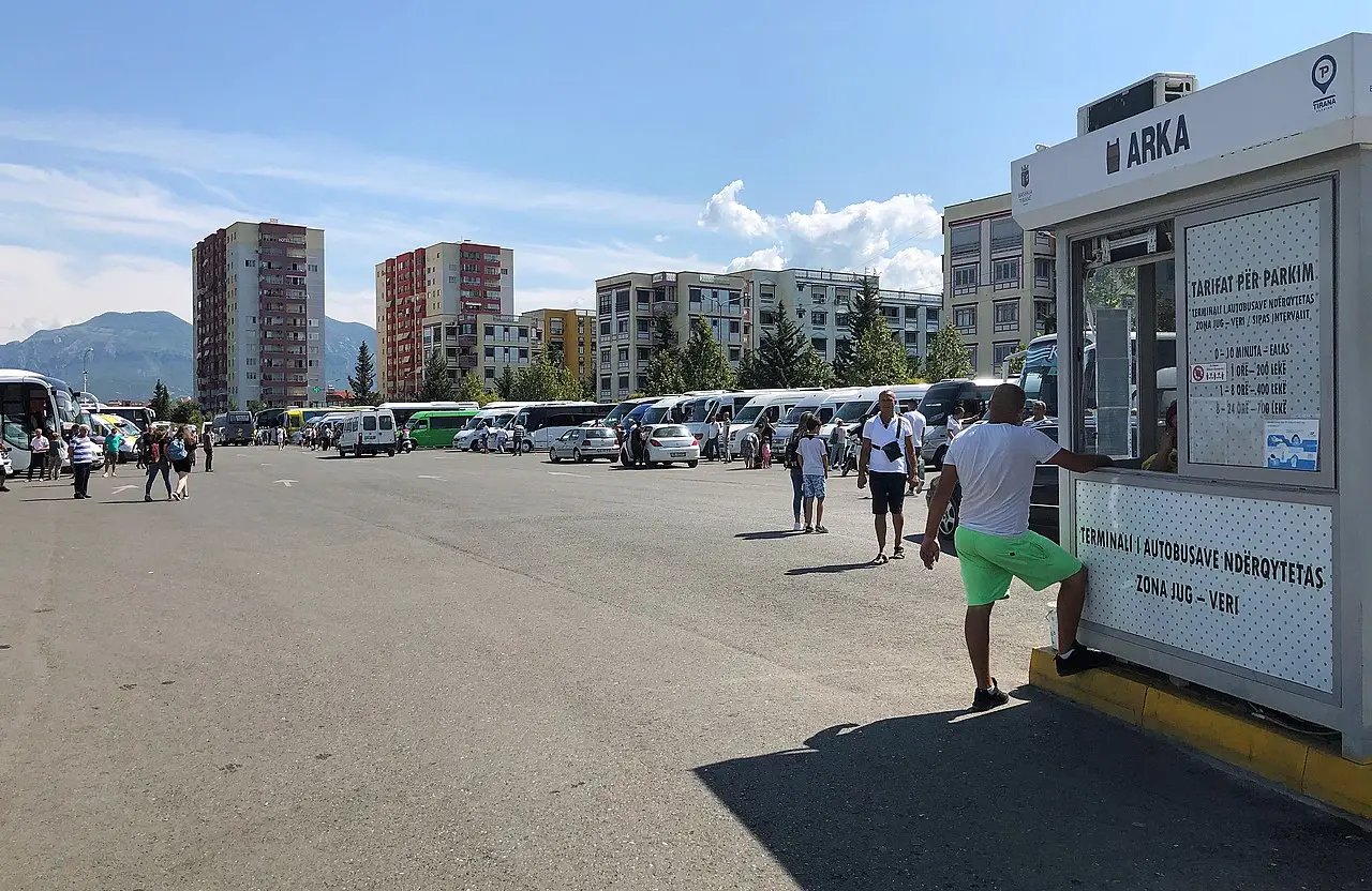 Minibuses and coaches parked at Tirana's intercity bus terminal with a ticket kiosk