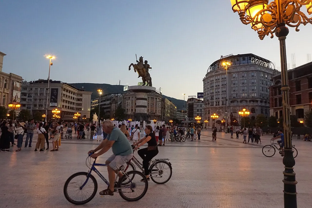 Macedonia Square in Skopje at dusk, with the Warrior on a Horse statue and cyclists crossing the square