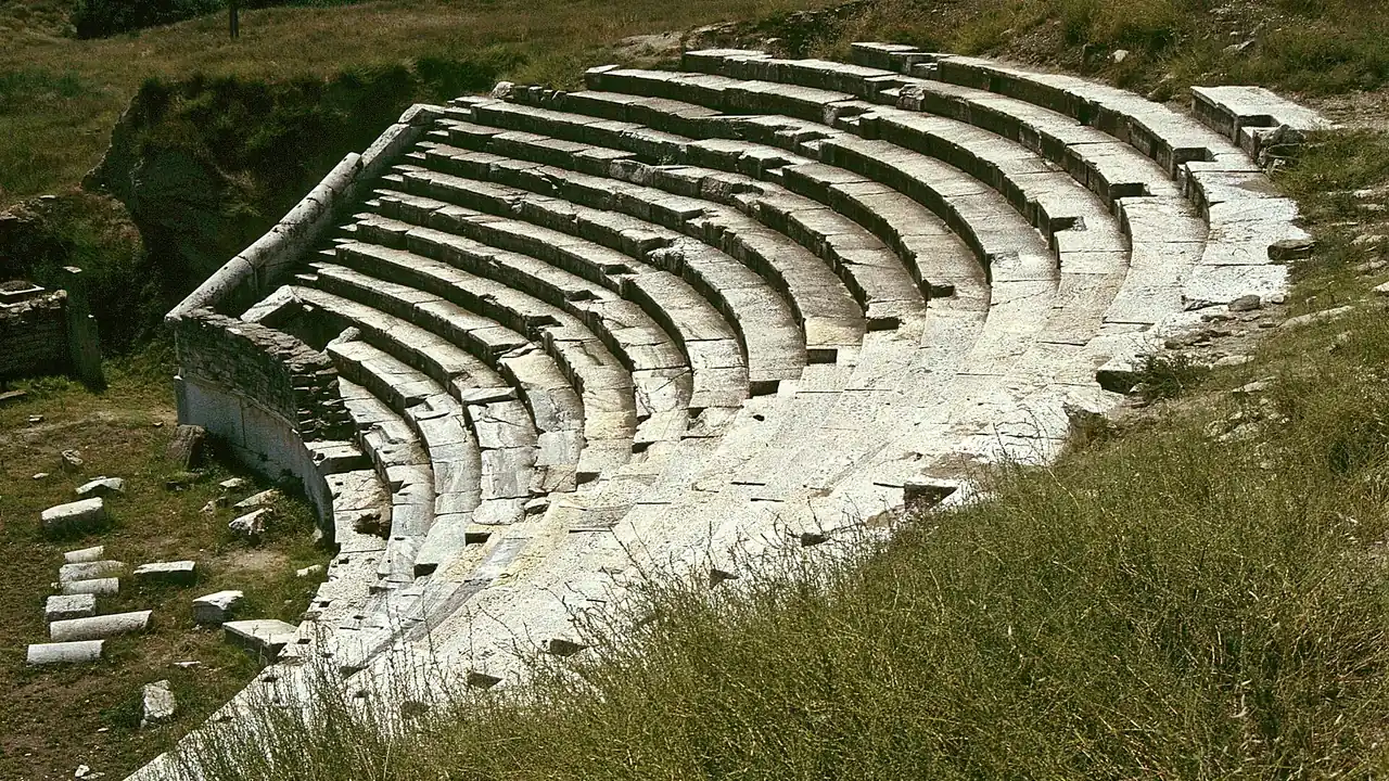 The curved stone seating rows of the Roman theatre at Stobi rising above the grass