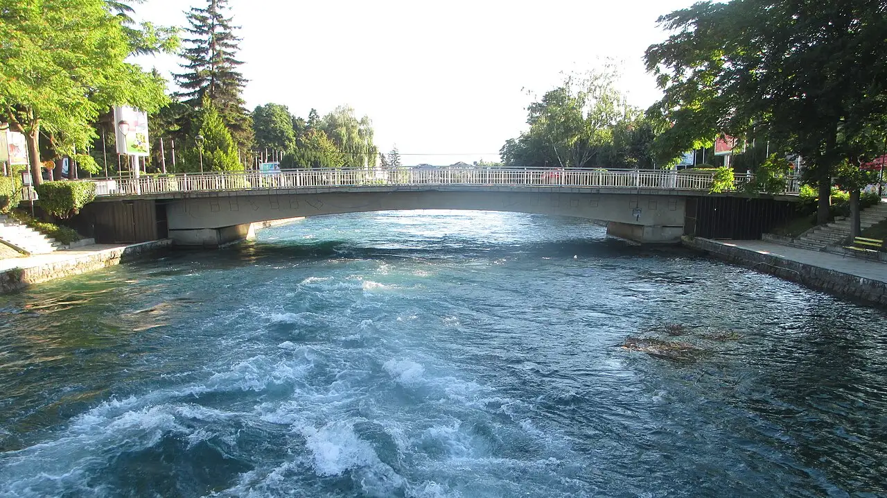 The turquoise Black Drin river rushing under a road bridge in the centre of Struga, with Lake Ohrid visible beyond