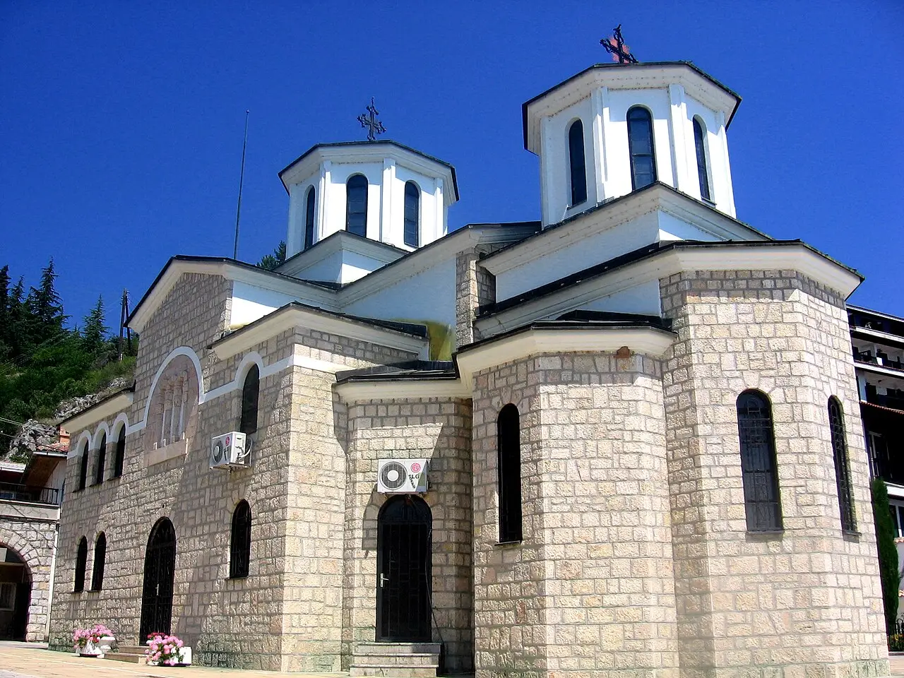 The stone church of Kalishta Monastery with twin white domes and cross finials against a deep blue sky, near Struga