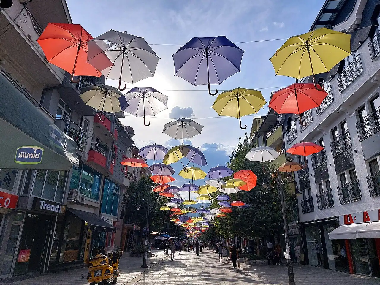 A pedestrian street in Struga shaded by dozens of brightly coloured umbrellas strung overhead, lined with cafés and shops