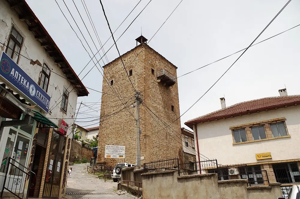 The tall stone Clock Tower of Kratovo rising above a street lined with small shops
