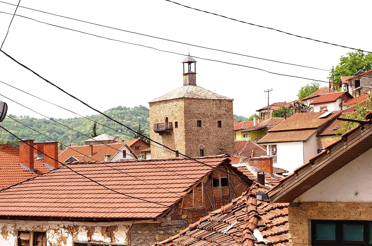 A view over the red-tiled rooftops of Kratovo with a stone defense tower rising among them and green hills behind