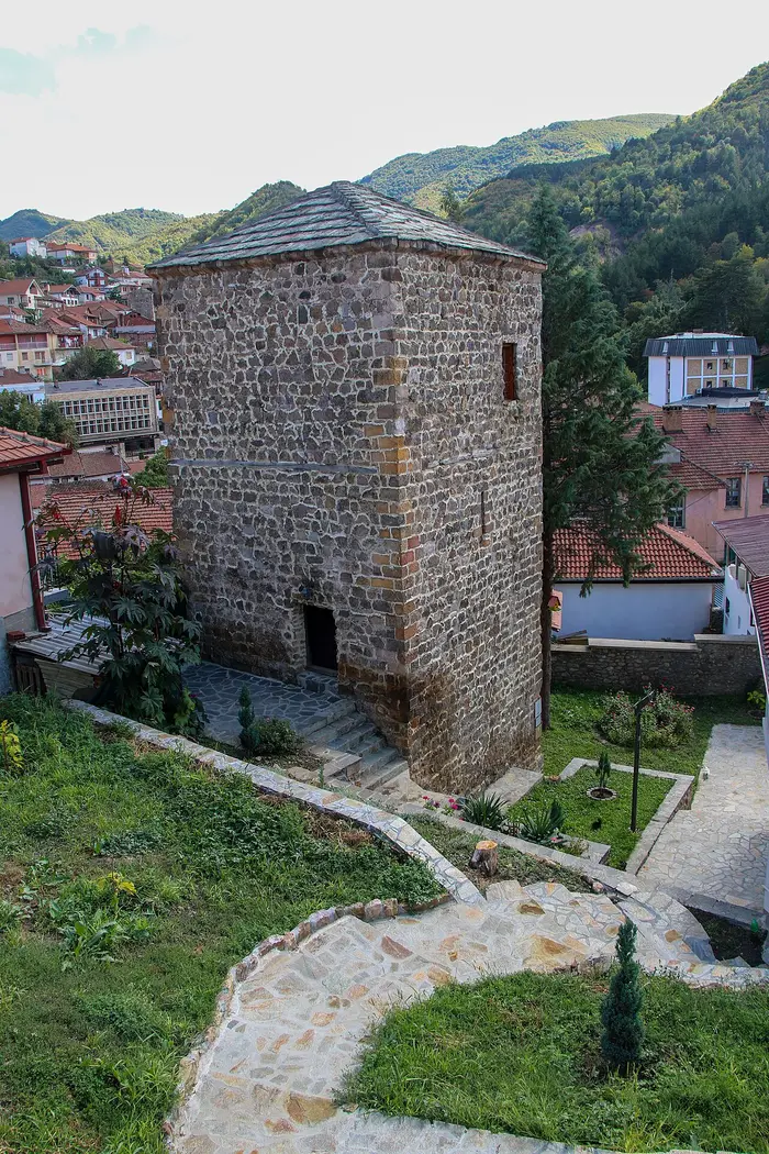 The restored square Zlatkov defense tower in Kratovo with its stone-tiled pyramidal roof, set in a garden