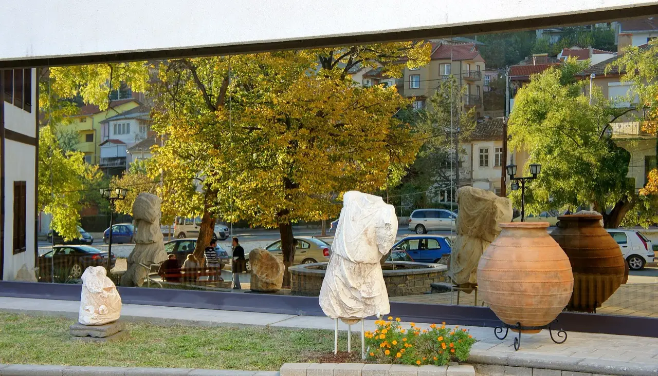 Roman-era stone statue fragments and a large clay amphora displayed outdoors in front of the Stip city museum