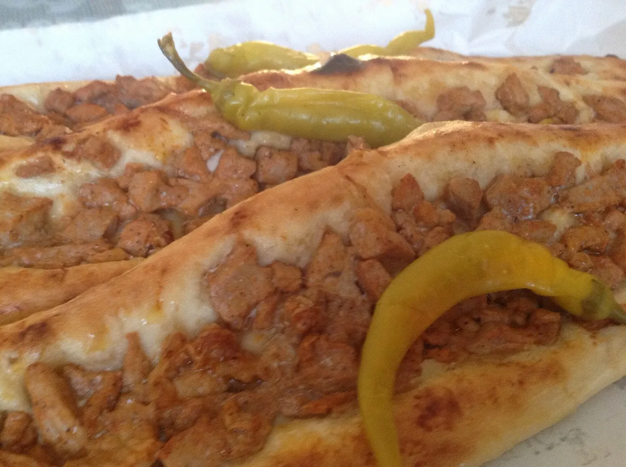 A close-up of pastrmajlija, an oval flatbread topped with diced cured meat and pickled peppers, fresh from the oven