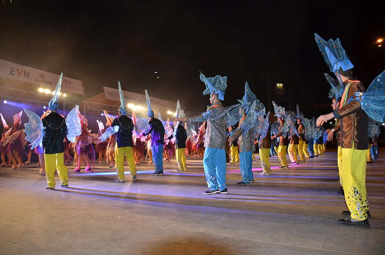 Costumed performers in glittering blue and yellow outfits dancing under stage lights at the Strumica Carnival