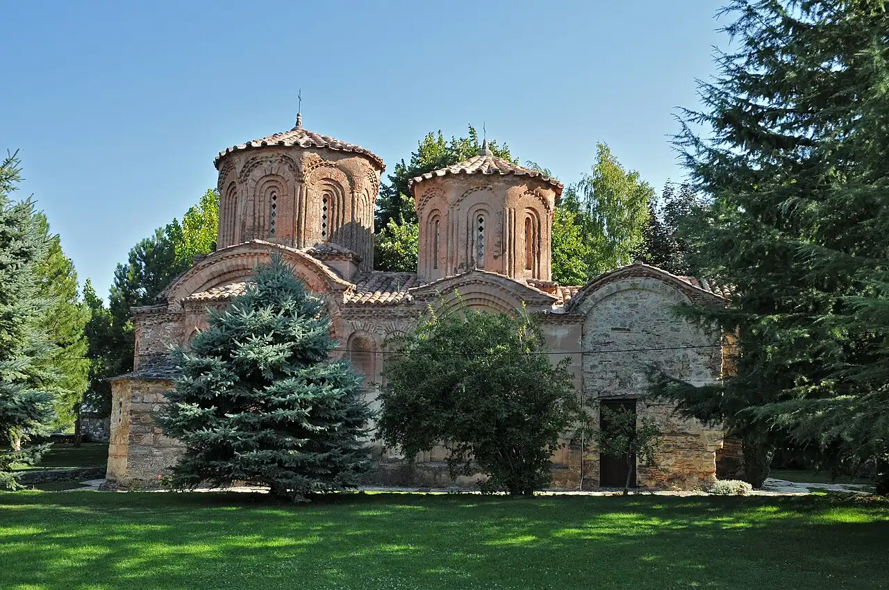 The domed brick church of the Veljusa monastery standing in a green garden with conifers around it