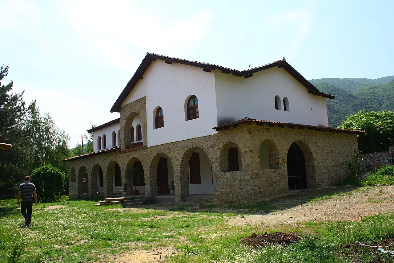 The stone and whitewashed monastery buildings of Vodoca with an arched loggia and green hills behind