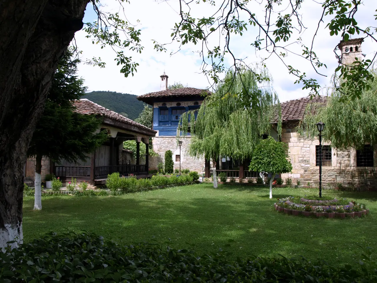 The garden courtyard of the Arabati Baba tekke with wooden lodge buildings and a tall tower among trees