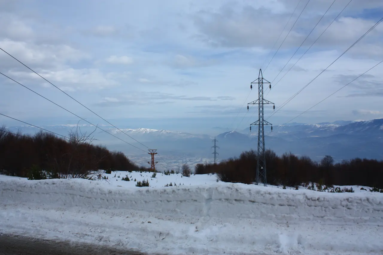 A snowy mountain road and ski-lift pylon at Popova Šapka in winter, looking down toward the valley